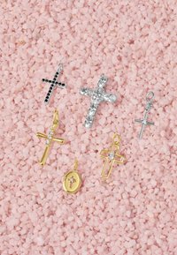 Guld- och silverkorspendanter med varierande designer, inklusive utsmyckningar och svarta accenter, arrangerade på en bakgrund av rosa salttextur.