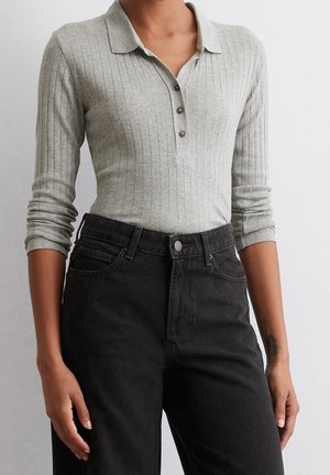 Osoba ubrana w jasnoszary prążkowany długi rękaw polo z guzikami, zestawiona z czarnymi dżinsami z wysokim stanem na jednolitym tle.