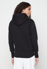 Schwarzer Hoodie mit Kapuze und Kordelzug, gerippten Bündchen und Saum. Glatte Textur und lässige Passform, von hinten vor einem neutralen Hintergrund betrachtet.