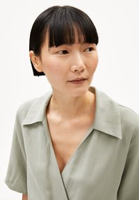 Light green collared shirt with short sleeves, featuring a deep V-neck and smooth texture, set against a plain white background.