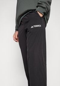 Schwarze Outdoor-Hosen mit Reißverschlusstaschen und Terrex-Logo. Hergestellt aus leichtem Material mit glatter Textur und taillierter Passform.