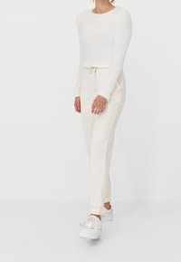 Bílý chlupatý top s dlouhým rukávem kombinovaný s krémovými tepláky s šňůrkou v pase a žebrovanými manžetami, doplněný bílými teniskami.