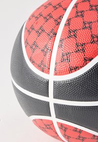 Közeli felvétel egy vörös és fekete panelekből álló, fehér vonalakkal elválasztott, texturált kosárlabdáról világos háttéren.