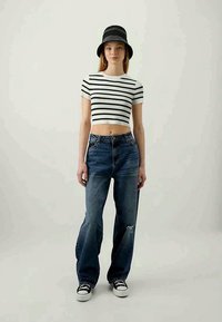 Striped cropped t-skjorte i hvit og svart; løse blå jeans med slitte detaljer; svart bøttehatt; svart og hvite joggesko.
