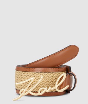 Cinturón de cuero marrón y tejido con hebilla tipo cursiva "Karl" en tono dorado, enrollado contra un fondo gris liso.