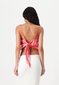 Raudona bandana stiliaus palaidinė su surišamu nugaros detalėmis. Su plonomis petnešomis ir paisley raštu. Nešiojama su tekstūruota balta sijonu.