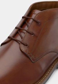 Chaussure habillée en cuir marron avec laçage fermé, coutures détaillées et surface lisse et polie sur fond blanc.