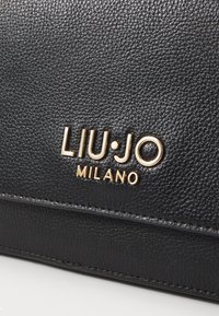 Borsa in pelle nera con texture, dotata del logo dorato impresso "LIU·JO MILANO" e di un dettaglio a cucitura orizzontale sul davanti.