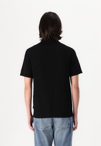 Svart kortermet polo skjorte med flat krage og sideslitser, kombinert med lyseblå denimjeans som har en avslappet passform.