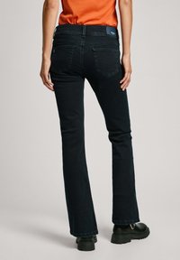 Zwarte flared jeans van denim, met een mid-rise taille, twee achterzakken en zichtbare stiksels. Draag met een effen oranje top.