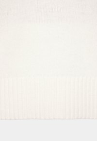 Gros plan d’un tissu tricoté blanc montrant un ourlet côtelé et une section supérieure à texture lisse.