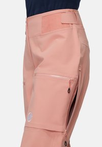 Rosa technische Hose mit hoher Taille, seitlichen Reißverschlusstaschen und dehnbarem Material. Über dem Bund befindet sich ein sichtbares Logo.