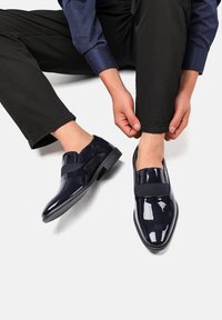 Zapatos de charol azul marino con una banda elástica en la parte superior, forma de punta cuadrada y una suela baja de goma negra.