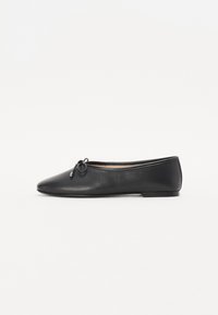 Ballerine en cuir noir avec un bout rond et un détail de nœud décoratif. Le design présente une texture lisse et un talon bas et plat.