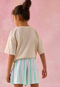 T-shirt en coton beige à manches courtes, associé à un short à rayures multicolores en vert pastel, rose et blanc. Une texture subtile est visible.