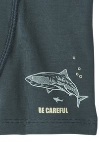 Dark fabric with shark illustration, bubbles, and text "BE CAREFUL" printed near the hem.