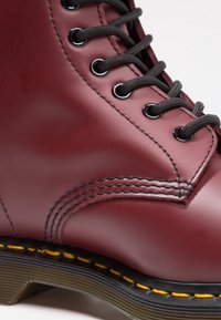 Botte en cuir bordeaux avec lacets noirs, œillets argentés, coutures jaunes et semelle translucide striée.