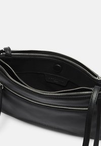 Borsa in pelle nera con cerniera argento, caratterizzata da una texture liscia e una fodera interna. Include un bottone a pressione e una tracolla regolabile.