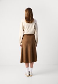 Brun knälång kjol med mjuk textur och utsvängd design, tillsammans med en ljusbeige sweatshirt och sneakers med silveraccent.