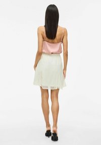 Haut en satin rose clair avec des bretelles fines, associé à une jupe blanche semi-transparente avec des fentes sur les côtés, et des chaussures à talons hauts noires.