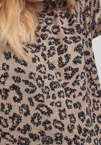 Un pull en tricot beige avec un imprimé léopard noir et des accents scintillants. Le tissu est doux au toucher et a une coupe décontractée.