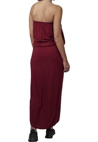 Viininpunainen maksimekko, jossa on elastinen hartioiden paljastava yläosa ja laskeutuva kangas, yhdistetty mustiin lenkkareihin rentoa ilmettä varten.
