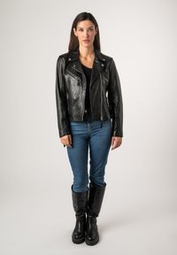 Zwarte leren motorjack met zilveren hardware, ritszakken en een asymmetrische kraag. Gepaard met blauwe jeans en zwarte kniehoge laarzen.