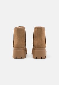 Bottes ankle en suède marron avec une semelle épaisse, dotées d'une finition lisse et de coutures visibles sur les côtés. Conçues pour un usage casual.