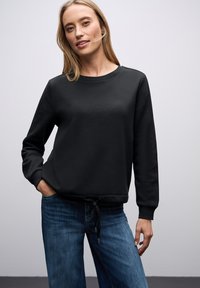 Felpa nera con maniche lunghe, collo a giro e vita arricciata. Abbinata a jeans di denim azzurri chiari. Tessuto morbido, design casual.