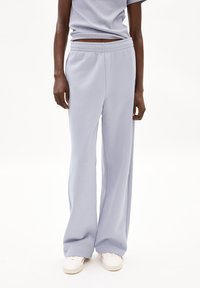 Pantalones de chándal lavanda claros con un corte holgado, cintura elástica y textura suave. Combinados con zapatillas blancas para un look casual.