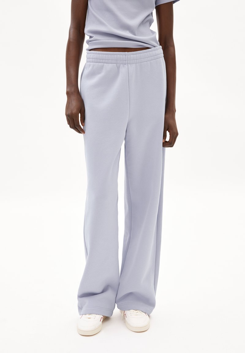 Pantalones de chándal lavanda claros con un corte holgado, cintura elástica y textura suave. Combinados con zapatillas blancas para un look casual.