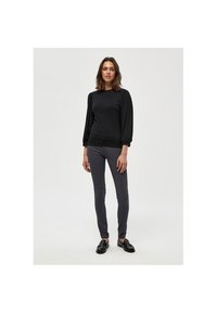 Sort ribbet langærmet skjorte med rund halsudskæring og voluminøse ærmer, parret med slim-fit grå bukser og sorte sko på en neutral baggrund.