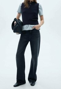 Czarne dżinsy o szerokich nogawkach z ciemnym bezrękawnikiem z dzianiny na jasnoszarej koszulce. Czarna torebka i buty na niskim obcasie dopełniają strój.