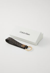 Porte-clés Calvin Klein en cuir noir avec des accents dorés et un design à motifs. Livré dans une boîte blanche avec le nom de la marque imprimé.