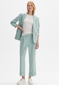 Completo menta chiaro composto da un blazer su misura e pantaloni abbinati con risvolti, abbinato a una maglia bianca con texture e sneaker bianche.