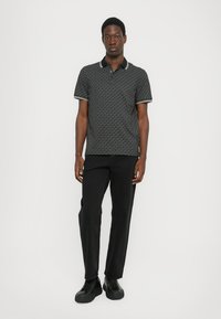 Polo noir avec un motif géométrique, bord de col blanc et manches courtes, associé à un pantalon noir et des baskets noires.
