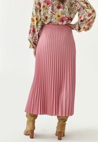 Falda rosa plisada hecha de material ligero, que llega a la mitad de la pantorrilla, combinada con botas de tacón marrones. Cuenta con una cinturilla y una textura fluida.