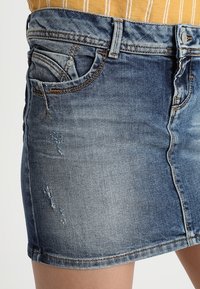 Denim minikjol i ljusblått med slitna detaljer, femficksdesign och en standard midja. Har ljus blekning och sömnadsaccenter.