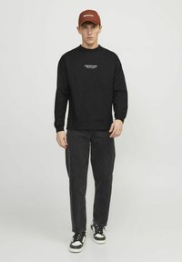 Svart långärmad skjorta med vit text, tillsammans med mörka jeans och svart-vita sneakers. Brun keps med vit logotypdetalj.