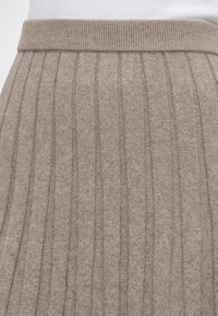 Jupe beige en maille côtelée avec une large ceinture portée sur un haut blanc.