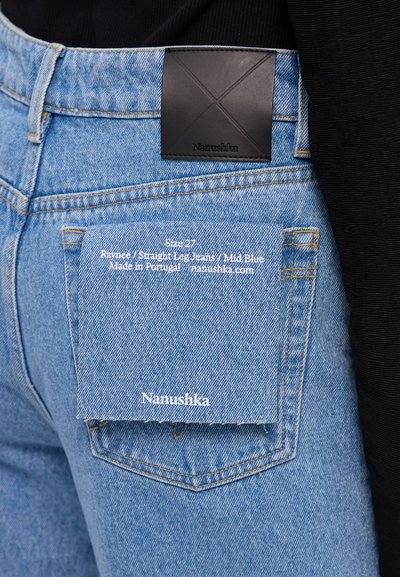 Mid-blauwe rechte jeans met een zwart leren logo patch op de tailleband en een wit label op de achterzak.