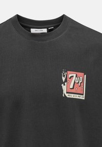 Sort bomulds T-shirt med et retro 7-Up logo trykt i rød og creme, rund halsudskæring og korte ærmer. Blød, glat tekstur.