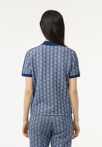 Sininen kuviollinen polo-paita, jossa on geometrisia muotoja, lyhyet hihat ja ribatattu kaulus, yhdistettynä samanlaisiin kuviollisiin housuihin.