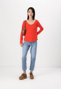 Röd långärmad V-ringad topp, ljusblå raka jeans och bruna plattformsskor. Brunt axelremsväska, slät tyg och avslappnad passform.