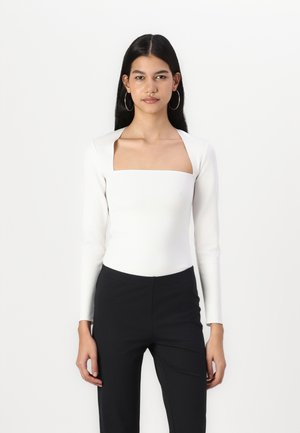 White long-sleeve top with a square neckline, paired with black trousers. Smooth texture, form-fitting design, minimalistic style.