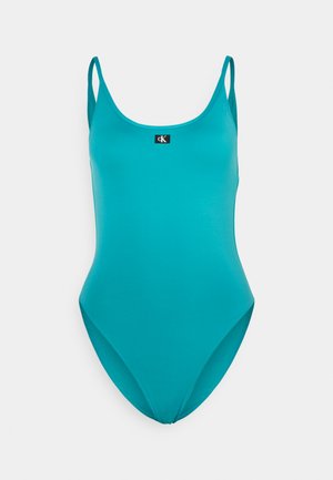 Maillot de bain une pièce turquoise avec bretelles réglables, décolleté haut et un petit logo noir au centre devant. Tissu doux et extensible.