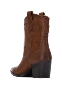 Bota de cowboy de cuero marrón con detalles bordados, punta ligeramente afilada y tacón negro apilado. Dispone de lengüetas para facilitar su colocación.