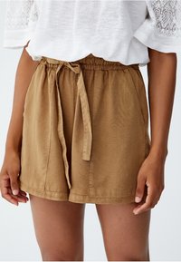 Shorts marron légers avec une ceinture élastique et un cordon de serrage, dotés de deux poches latérales et d'un tissu lisse et texturé.