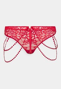 String rouge en dentelle avec des motifs floraux, des bords festonnés et des chaînes décoratives avec des accents ronds. Design arrière ouvert avec une fermeture éclair centrale.