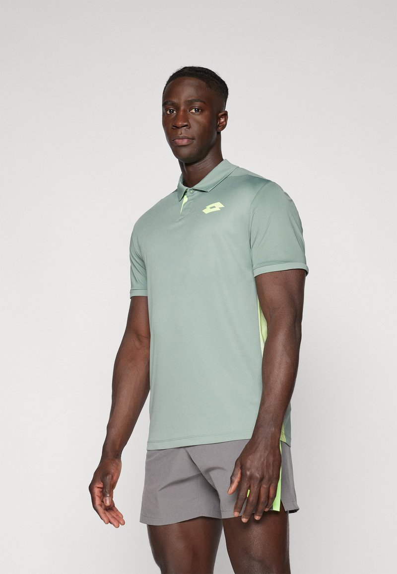 Lysegrøn polo t-shirt med et gult logo, kombineret med grå shorts. Har en knaplukket krave og korte ærmer. Fremstillet af glat stof.